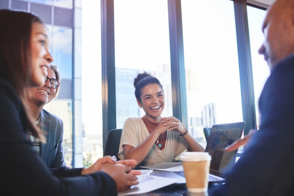 Grupa profesjonalistów śmiejąca się i rozmawiająca podczas spotkania z widokiem na miasto w tle.